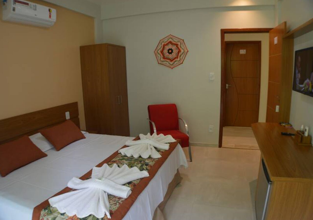 A hotel room with a bed, a red chair, a wooden wardrobe, and a wall decoration.