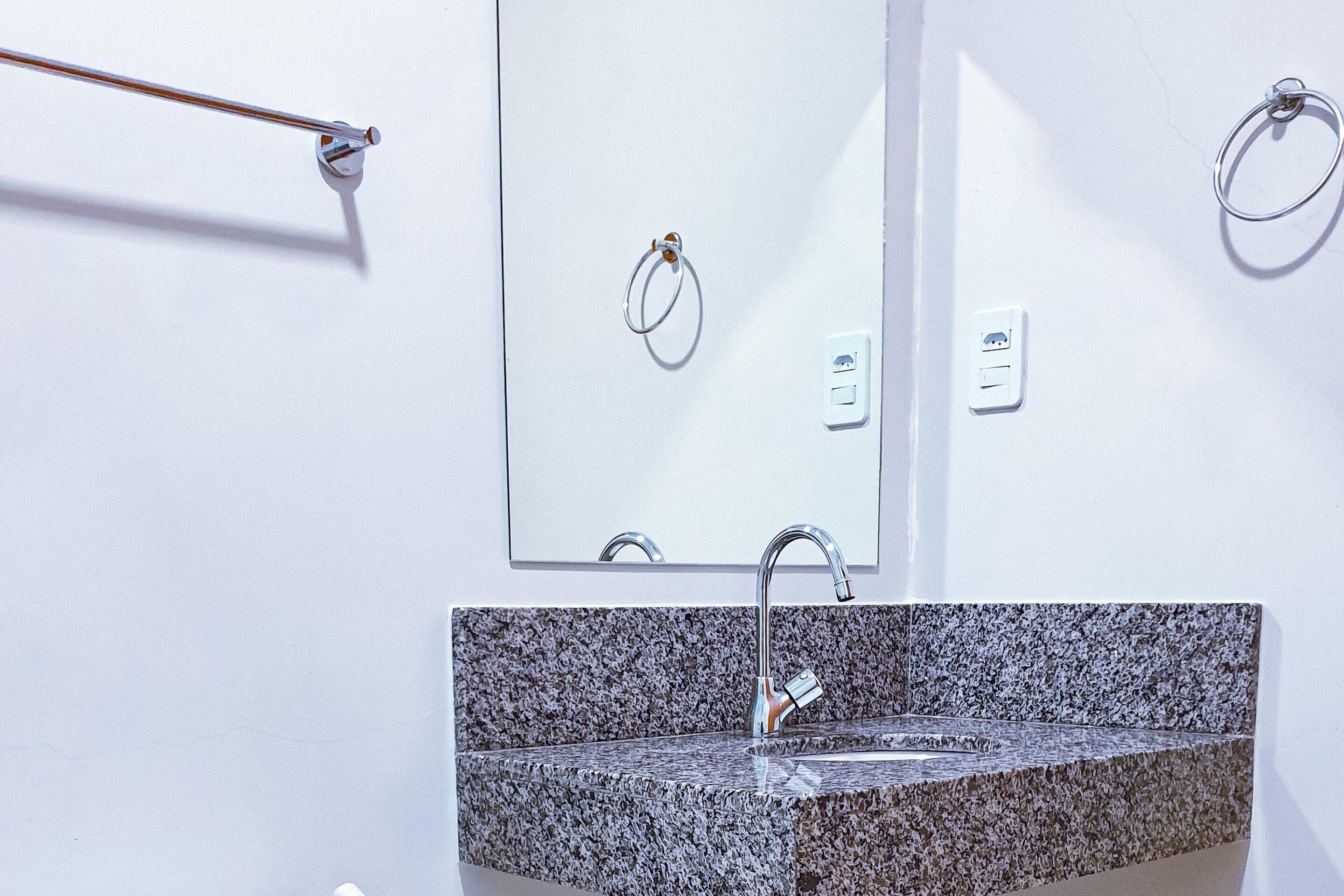 A bathroom with a granite sink, a mirror, and towel rings.