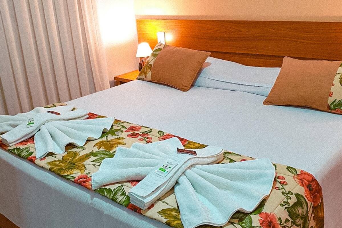 A neatly made bed with floral bedding, a wooden headboard, and a nightstand with a lamp.