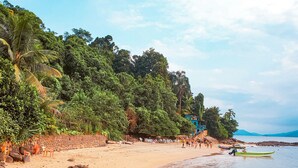 Una playa con costa rocosa, un bote pequeño y algunas personas.