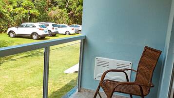 Varanda com cadeira de vime, radiador branco e vista para carros estacionados numa área ajardinada.