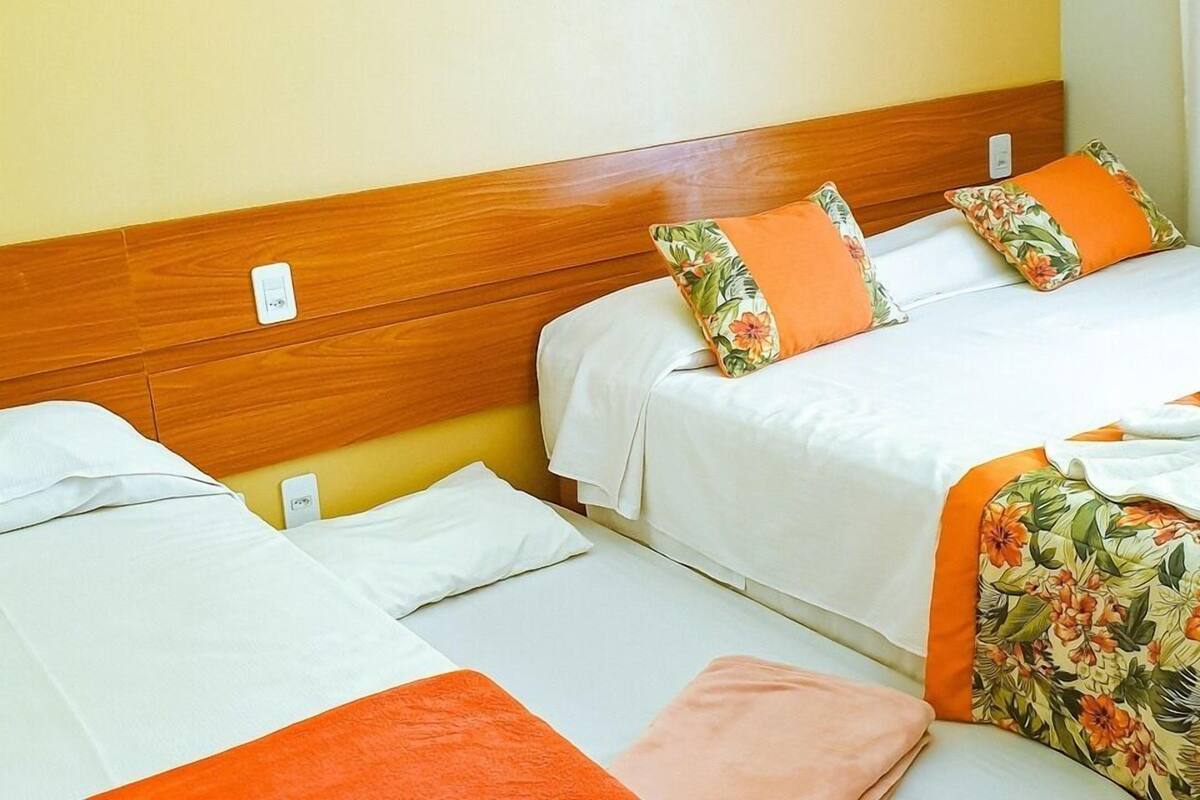 A hotel room with two beds, each with white bedding and orange accents.