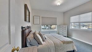 A bedroom with a bed, a dresser, a window with blinds, and a door with a brass handle. - 230 4th Street (Ashland)