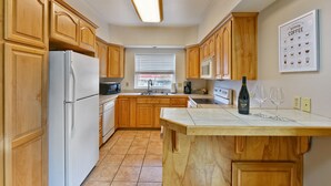 A kitchen with wooden cabinets, a white refrigerator, a microwave, and a wine bottle on the counter. - 230 4th Street (Ashland)