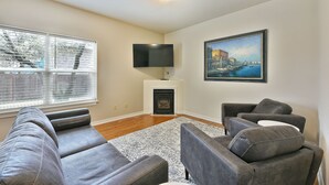 A living room with a fireplace, a flat-screen TV mounted above it, and a painting on the wall. - 230 4th Street (Ashland)