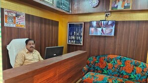 Un área de recepción con un escritorio de madera, un sofá estampado con motivos florales, un televisor montado en la pared y un reloj.