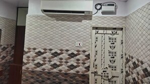 Una habitación con un muro de azulejos con diseño, una puerta blanca con indicaciones de emergencia y una unidad de aire acondicionado instalada en el techo.