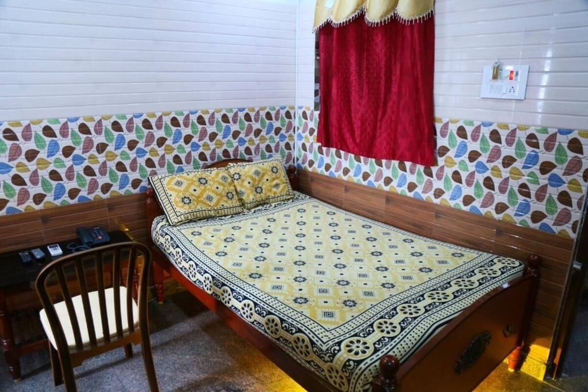 A small, cozy room with a bed, a chair, and a window with a red curtain.
