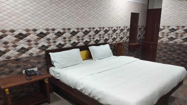 Una cama bien hecha con sábanas blancas en una habitación con paredes de baldosas estampadas y un cabecero de madera.