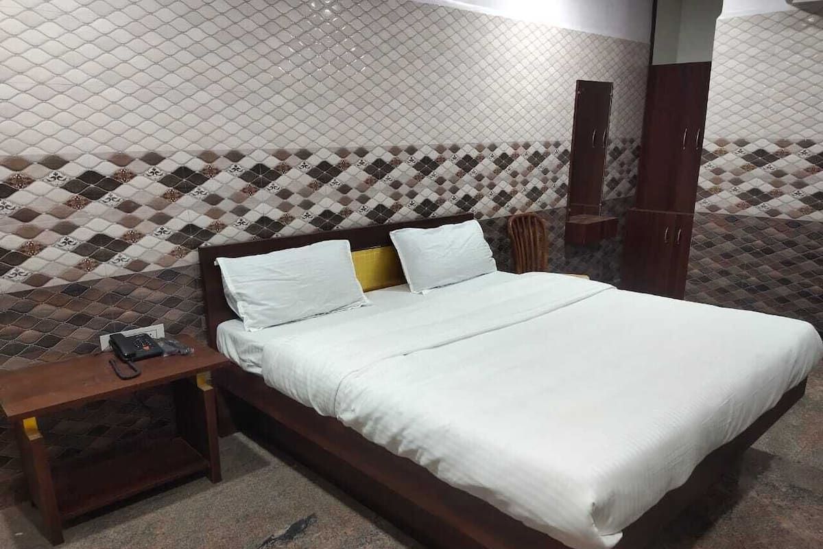 A neatly made bed with white linens in a room with patterned tile walls and a wooden headboard.