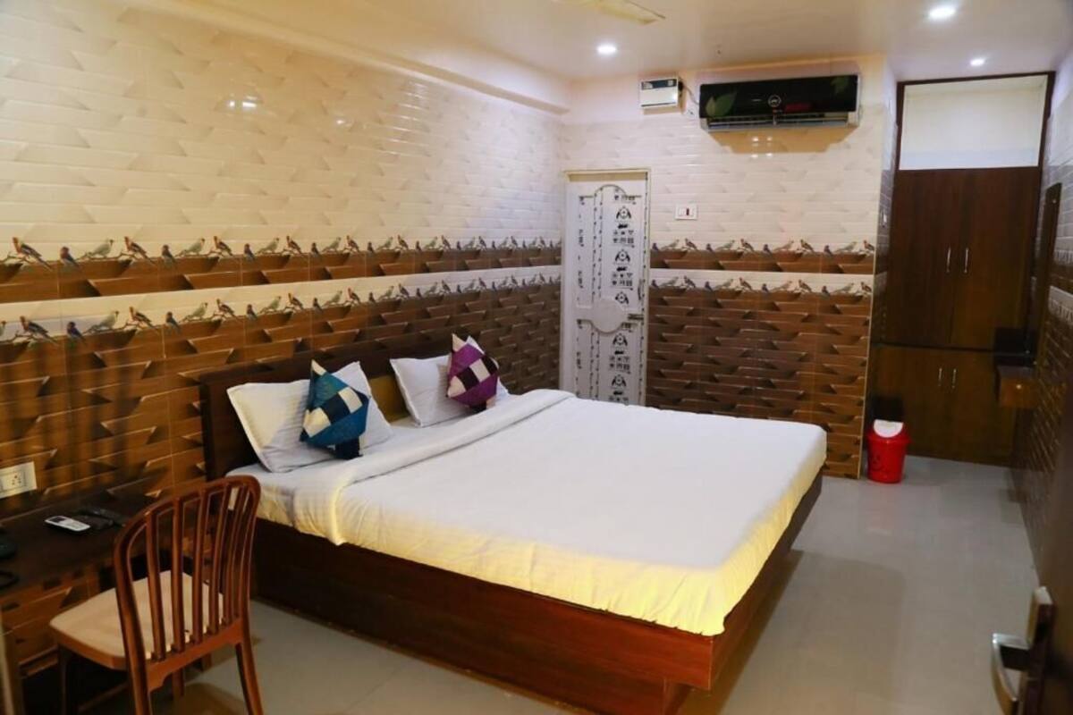 A bedroom with a bed, a desk, a chair, a wardrobe, and a wall-mounted air conditioning unit.