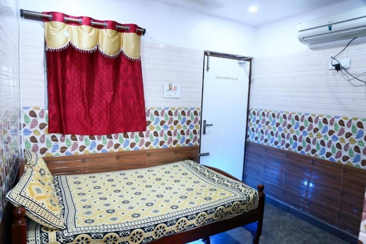 A room with a bed, a red curtain, a patterned wall, and an air conditioning unit.