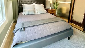 Un dormitorio con una cama grande, un ventilador de techo, una mesita de noche con lámpara y una puerta corrediza de cristal.