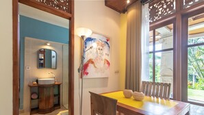 Une salle de bain avec un lavabo, un miroir et un meuble en bois. Il y a un tableau au mur et une fenêtre avec des rideaux.