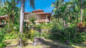 Un complexe hôtelier tropical doté d’un grand bâtiment avec un toit rouge et de nombreux balcons, entouré d’une végétation luxuriante et de palmiers.