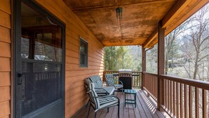 A wooden porch with a sliding glass door, two striped chairs, a small table, and a grill. - Nuttin Better - App Ski Mtn cabin with hot tub, game table (Blowing Rock)
