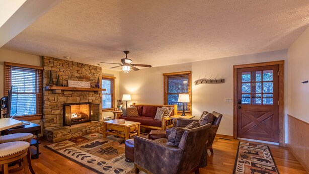A cozy living room with a stone fireplace, wooden furniture, and a large window with blinds. - Nuttin Better - App Ski Mtn cabin with hot tub, game table (Blowing Rock)