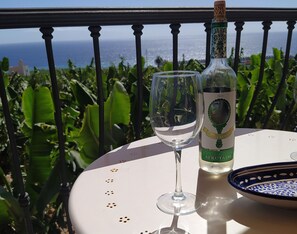 A bottle of wine and a glass on a table with a view of the ocean.