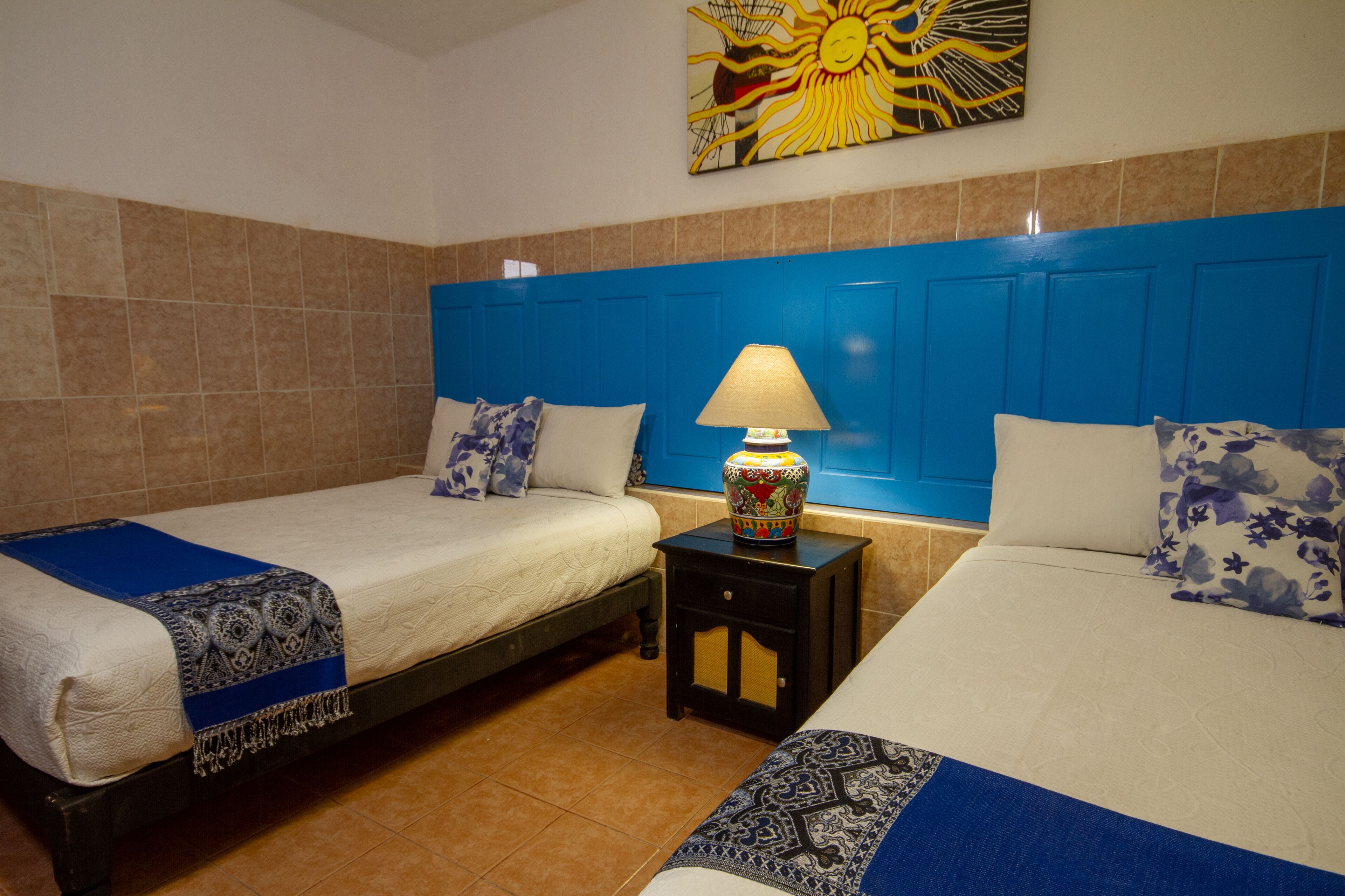 A hotel room with two beds, a nightstand with a lamp, and a wall painting.