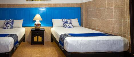 A hotel room with two beds, a blue headboard, a nightstand with a lamp, and a painting on the wall.