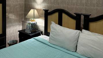 A hotel room with a bed, a nightstand with a lamp, and a trash bin.
