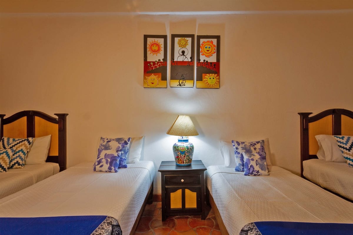 A hotel room with two beds, a nightstand with a lamp, and wall art above the beds.
