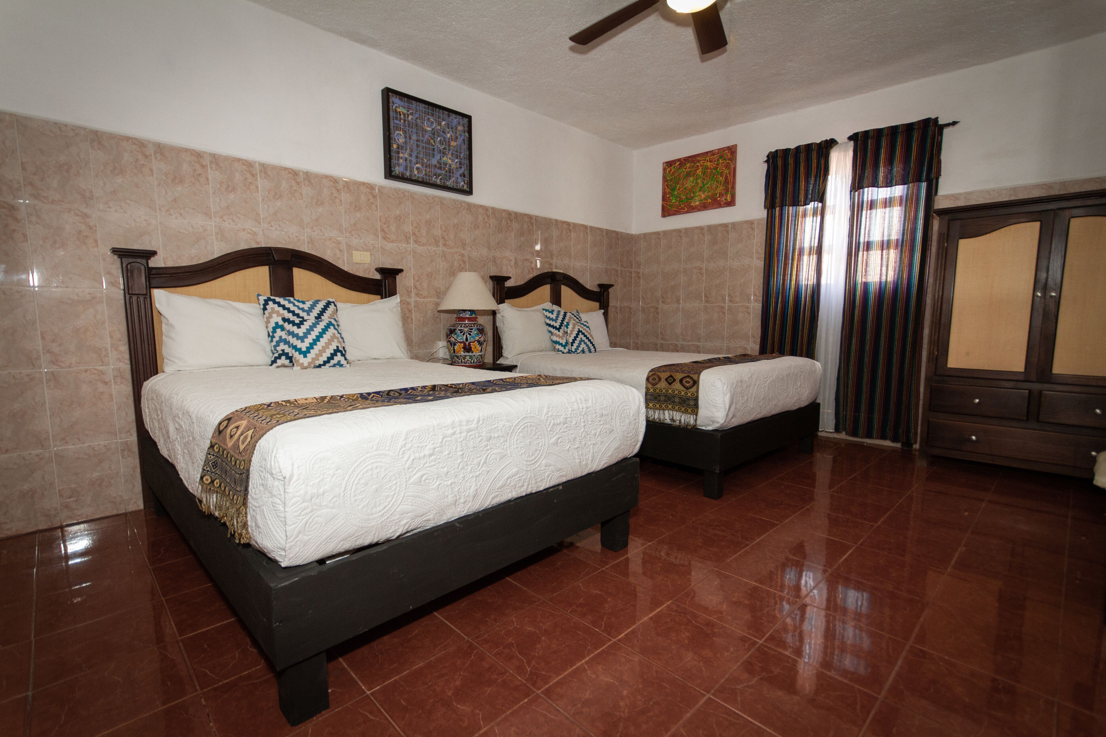 A hotel room with two beds, a ceiling fan, and a wardrobe.