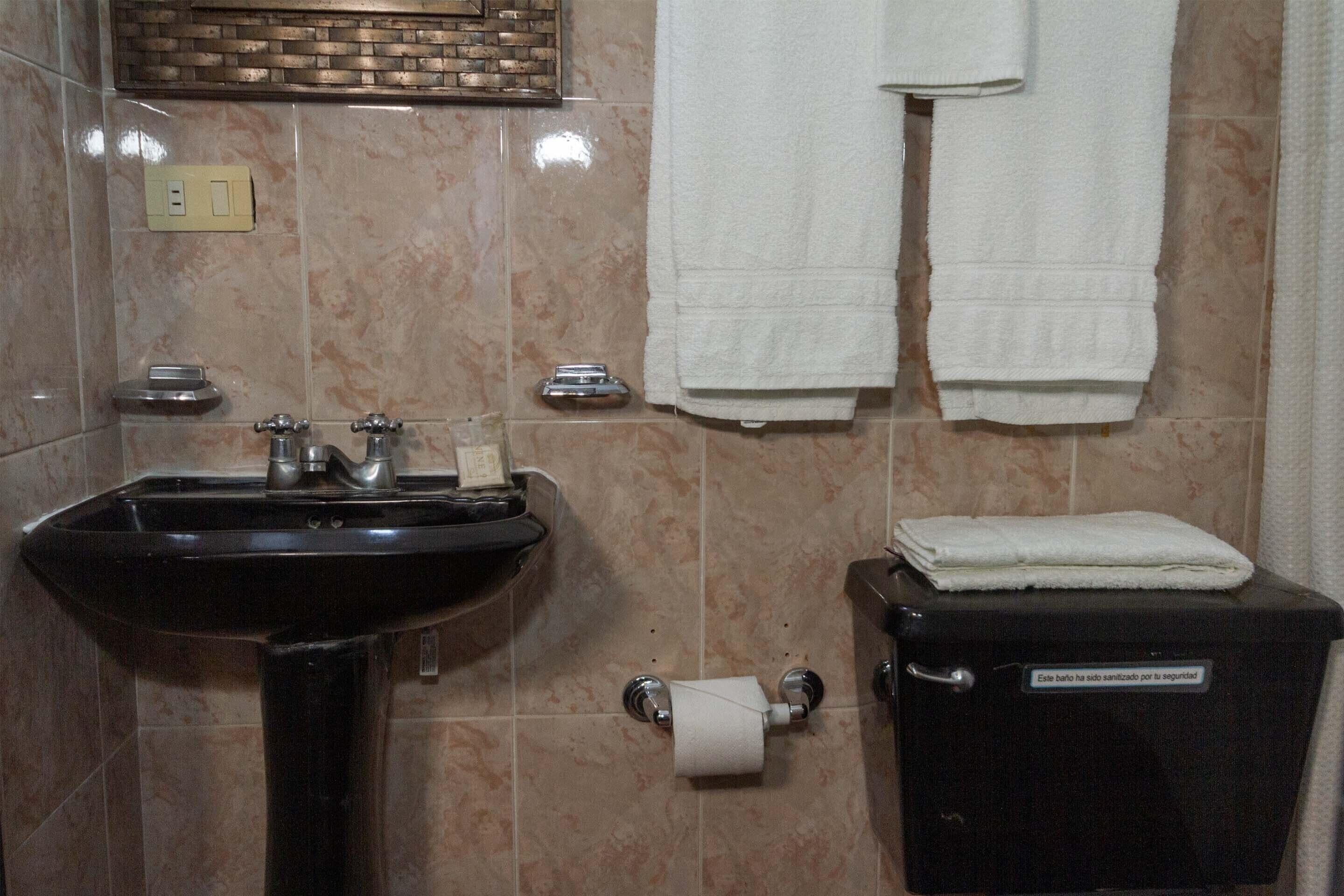 Een badkamer met een wastafel, twee kraanwerk, een toilet en een handdoekhouder met twee witte handdoeken.