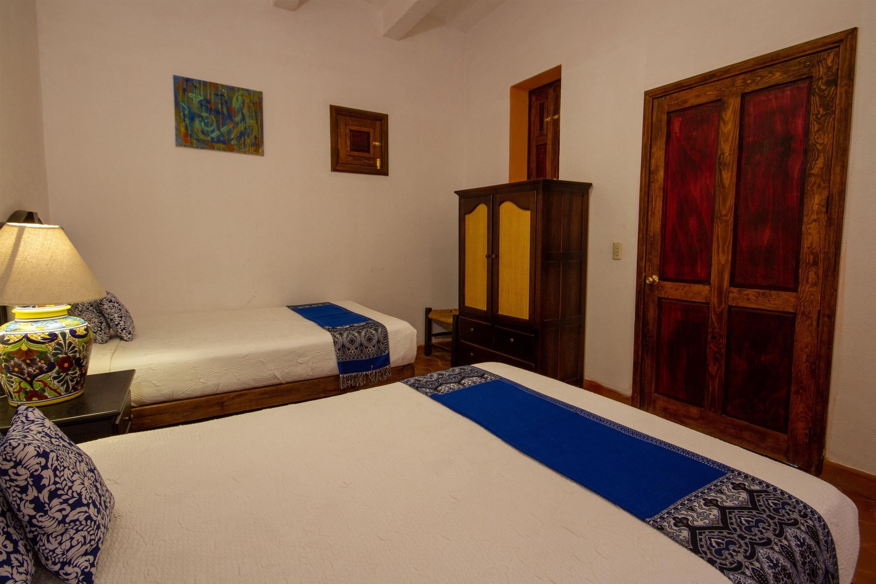 Una habitación de hotel con dos camas, un armario de madera, un espejo y una lámpara decorativa.