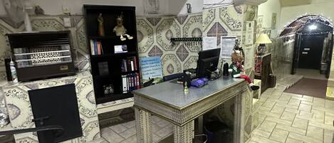 Una habitación con suelo de baldosas, un escritorio con ordenador, una estantería y una estatua decorativa.