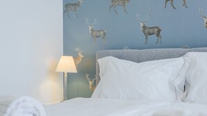 Ein ordentlich bezogenes Bett mit weißen Leinen, einem grauen Kopfteil und einer Wand mit einem Hirschmuster.