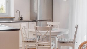 Eine moderne Küche mit weißen Schränken, einem Edelstahlkühlschrank und einem Essbereich mit weißen Stühlen.