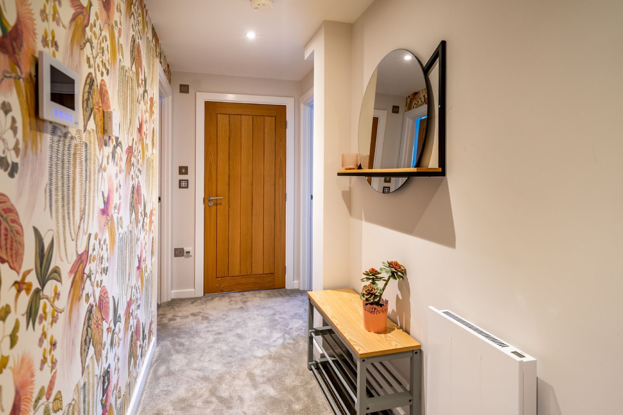 Un couloir avec une porte en bois, un miroir au mur, une petite table avec une plante et un radiateur.