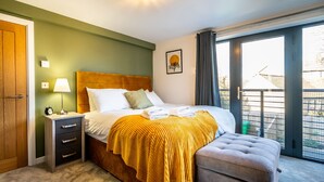 Habitación de hotel con cama, mesita de noche, lámpara, banco y ventana con vistas al exterior.