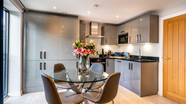 Una cocina moderna con gabinetes grises, una mesa de comedor de vidrio y un jarrón con flores.