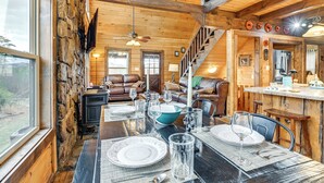 A wooden interior with a dining table set for four, a fireplace, and a staircase leading to an upper level. - Mtn Views, Yard, & Fire Pit: Multi-Level Cabin (Franklin)