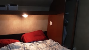 Een bed met een gestreept dekbedovertrek, een rood kussen en een houten garderobe met spiegel.