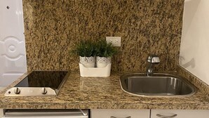Una cocina con encimera de granito, pileta de acero inoxidable, horno empotrado y muebles de cocina blancos.