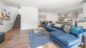 Een moderne woonkamer met een blauwe bank, een glazen salontafel en een trap naar een verdieping erboven.