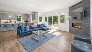 Een moderne, open woon- en eetruimte met een blauwe bank, een glazen salontafel en een open haard.