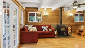 Un salón acogedor con un sofá rojo, paredes de madera, una chimenea y vistas amplias a través de grandes ventanales.
