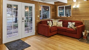Una habitación acogedora con un sofá rojo, paredes de madera y ventanas amplias con vistas al exterior.