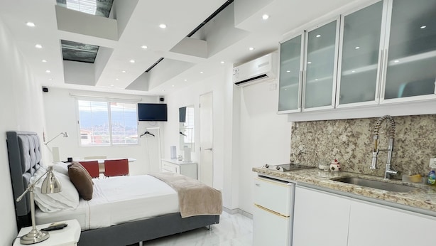 Une chambre d’hôtel moderne, équipée d’un lit, d’une table de chevet, d’une lampe et offrant une vue sur la ville par la fenêtre.
