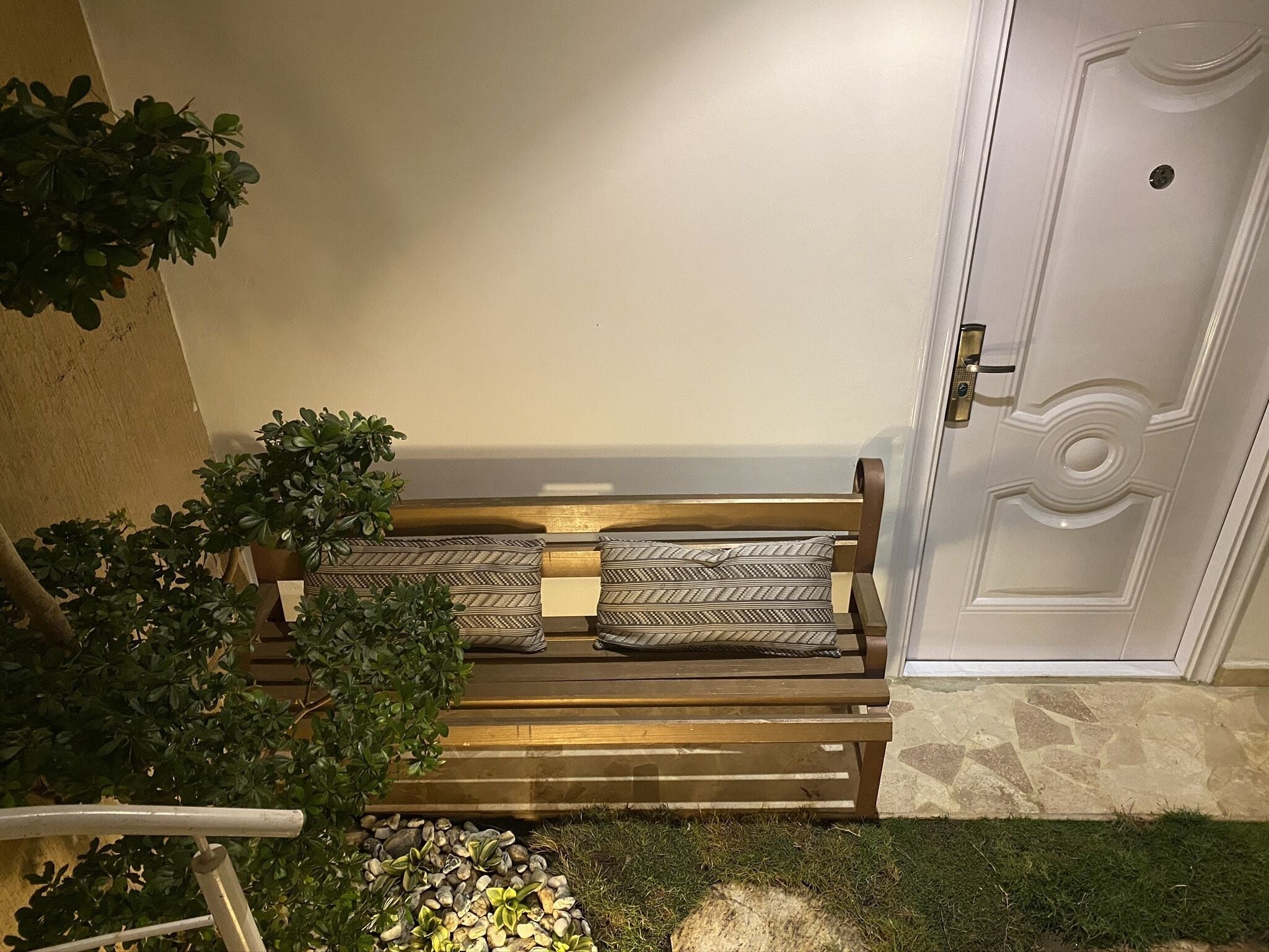 A wooden bench with patterned cushions, a potted plant, and a door with a keyhole.