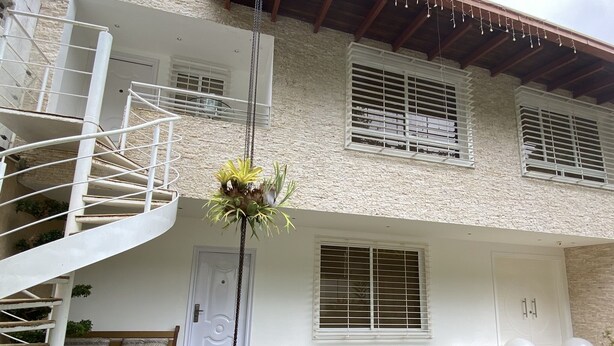 A two-story building with a white exterior, a spiral staircase, and a front door. - A house with views in Caracas in a safe area I (Caracas)