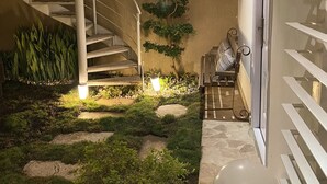 Un escalier en colimaçon menant à un balcon, un petit coin salon avec une table et des chaises, et une plante en pot.