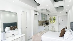A modern bedroom with a large bed, a bedside table, a mirror, and a built-in kitchen area with a window. - A house with views in Caracas in a safe area I (Caracas)