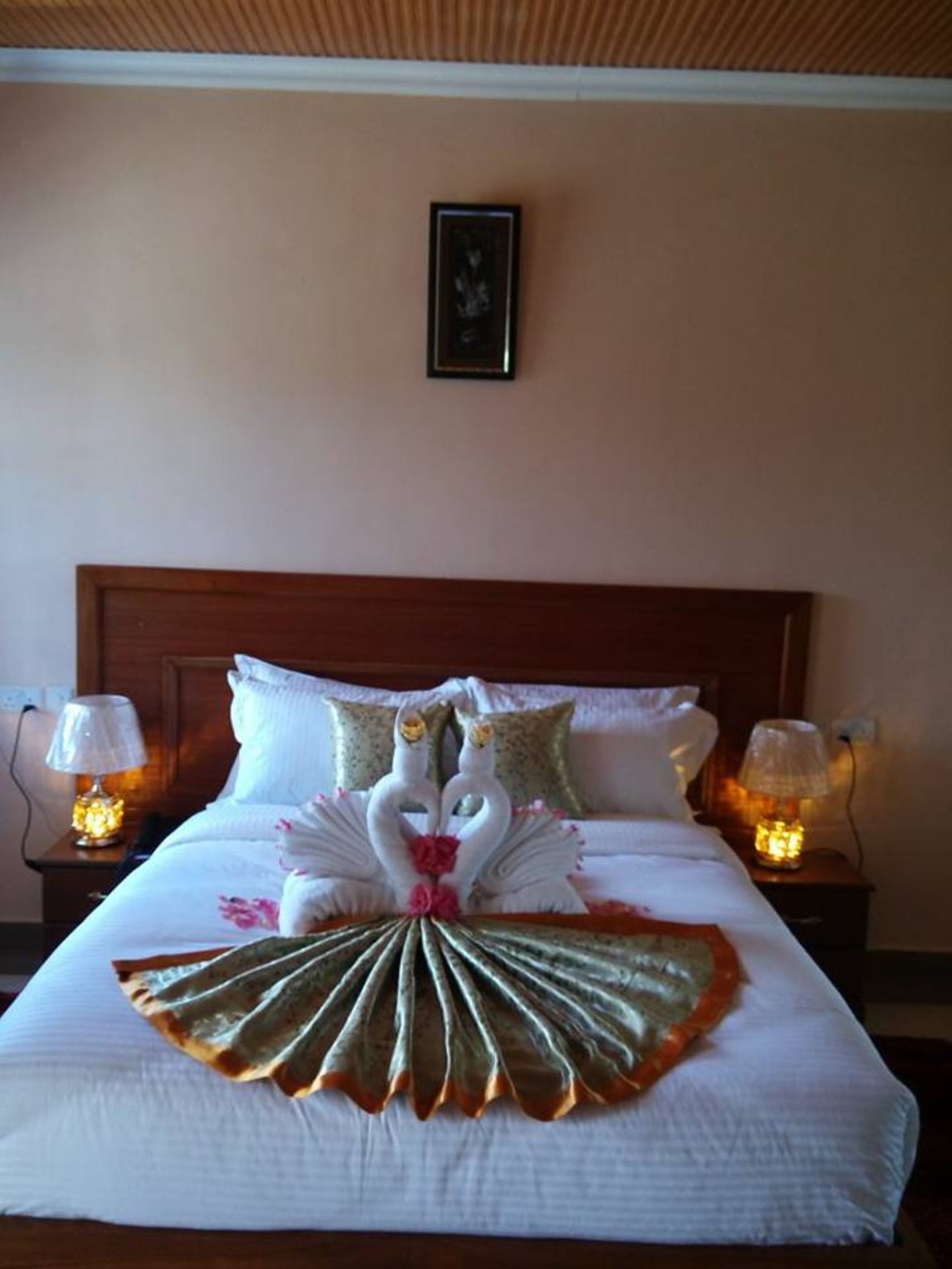 A hotel room with a neatly made bed, two lamps on either side, and a framed picture on the wall.