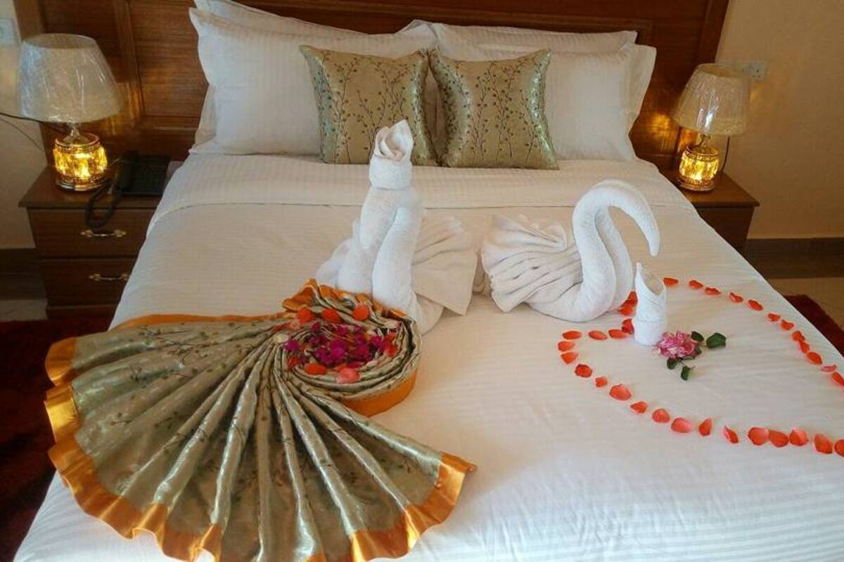 Ein ordentlich bezogenes Bett mit einer Schwan-Handtuch-Arrangement, einem Ventilator mit Blumen und Rosenblüten auf dem Bett.