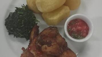 A plate with fried chicken, fried plantains, greens, and a small bowl of sauce.